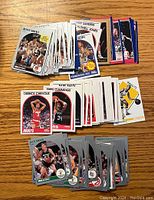 Photo showing multiple stacks of basketball trading cards spread out on a wooden surface, featuring various players and teams.