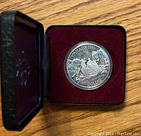 Silver coin in presentation box showing canoe scene and date 1989