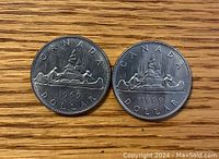 Two 1969 Canadian one dollar coins showing the canoe with voyageurs side on wooden surface