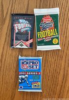 Front view of three sealed football card packs: 1991 Upper Deck, 1990 Fleer Premier Edition, and 1991 Pro Set Series 1.