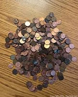 Pile of mixed Canadian and American pennies on a wooden surface showing a variety of colors, wear levels, and different coin years and designs.