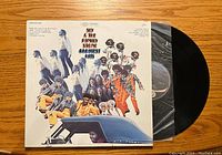 Top down view of the front cover of the vinyl record album featuring the band's name and colorful group photo with images of band members and car.