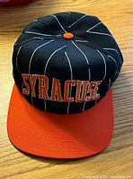 Front view of the black Syracuse Orangeman hat with orange brim, white pinstripes, and embroidered Syracuse text.