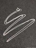 Full view of delicate 16 inch chain made of 10K gold lying flat on black surface, showing chain links and clasp