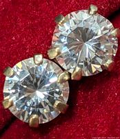Close-up photo of the two 10K gold stud earrings with round clear cubic zirconia stones on a red fabric background.