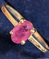 Close-up front view of 10K gold ring with oval ruby gemstone on blue background.