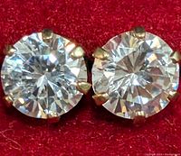Close-up of a pair of round clear cubic zirconia stud earrings set in 10K yellow gold four-prong settings on red background.