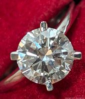 Top view of the ring showing the round brilliant diamond in six-prong setting on a polished band against red background