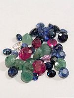 Close-up of loose genuine emerald, ruby, and sapphire gemstones showing various shapes and sizes with good clarity.