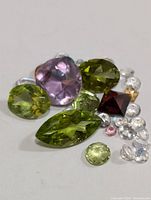 Close-up photo of assorted genuine faceted gemstones of various cuts and colors including amethyst, peridot, garnet, and clear quartz approximately 10 carats total.