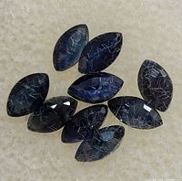 Top view of eight marquise cut dark blue sapphires on a light surface showing needle-like inclusions.