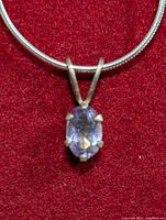 Close-up photo of oval amethyst pendant set in silver prongs on silver snake chain against red velvet background.