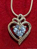 Front view of silver heart-shaped pendant with blue topaz gemstone and snake chain on red background.