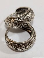 Close-up image of the pair of silver hoop earrings showing detailed floral and geometric engraved patterns on the metal.