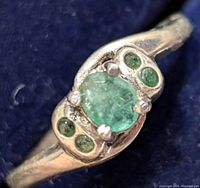 Close-up of the ring face showing central emerald and four smaller emerald stones in silver setting.
