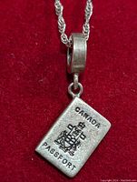 Close-up front view of the silver necklace with Canadian passport pendant on a red background.