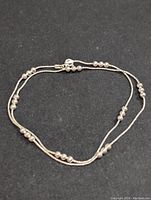 Full view of silver necklace laid flat showing beaded segments and clasp on black background.