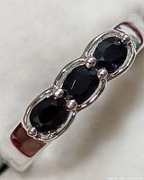 Close-up front view of silver ring showing three oval-shaped faceted dark blue sapphire stones in a chain-like prong setting on polished silver band.
