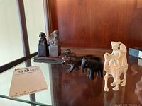 Two stone chop stamps with lion and dragon carvings on wooden tray, with carved ball detail, displayed with wooden animal figurines including a tiger, elephant, and camels with riders.