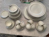 Overall view of stacked Aynsley Princelea white china pieces showing dinner plates, cups, saucers, bowls, and smaller plates with gold vine trim and embossed spiral texture on edges.