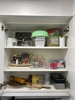Full view of cabinet shelves with baking accessories including measuring cups, cookie cutters, pans, rolling pins, and miscellaneous baking tools