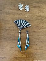 Sterling silver dragon design earrings paired with a fan-shaped brooch and a pair of turquoise drop earrings with geometric inlay on a wood surface.
