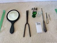 Full view of the lot: ebony mirror, iron tool, thimbles, hooks, glass items.