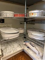 Multiple Corningware and ceramic baking dishes on two shelf levels including floral pattern and white ribbed pieces plus mandolin slicer in plastic bag