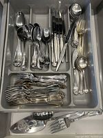 Drawer with assorted forks, knives, teaspoons, tablespoons, serving spoons, and serving forks with decorative handles.