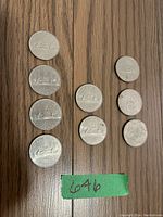 Top view of nine Canadian dollar coins arranged in columns on wood surface with green tape marker.