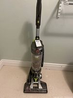Full view of Hoover WindTunnel upright vacuum cleaner with handle, hose attachment, gray and green colors, visible dust in container