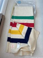 Folded Hudson's Bay blanket in clear packaging showing ivory wool and green, red, yellow and navy stripes