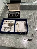 Full view of the assorted jewelry including rhinestone set, colorful brooch, pins, silver chains, and large linked bracelet.