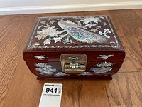 Front view of the jewelry box showing the peacock and floral mother of pearl inlay on the lid and sides, brass latch, and wooden base.