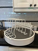 Photo showing one wire pan/pot lid holder in front of three Copco Lazy Susans stacked with black non-slip surfaces.
