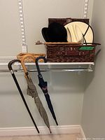 Four men's hats, three umbrellas, two wicker baskets on a shelf.