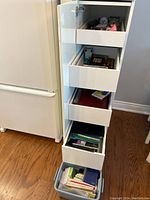 Open white shelving with multiple drawers filled with stationery and office items including notebooks, cards, and various paper supplies.
