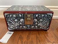 Front view of ornate mother of pearl inlaid jewelry box with brass lock showing floral vine patterns on dark red wood.