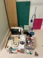 Photo showing Elna Air electric sewing machine with sewing accessories including scissors, threads, bobbins, pincushion, and rotary cutter with cutting mats in background.
