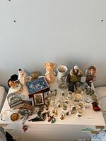 Full overview of all assorted trinkets, music boxes, clocks, and miniature figurines arranged on a white surface with a plain background.