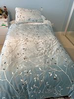 Twin bed made up with light blue comforter and matching pillowcase featuring leafy branch pattern