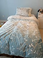 View of twin bed with bed linens showing blue to white gradient with silver leaf and branch design