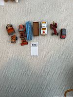 Overview showing all seven vintage metal toy vehicles lined up on carpet: 2 tractors, ambulance car, red car, trailer truck, and smaller toys.