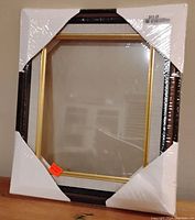 Front view of wrapped classic picture frame with protective corner covers showing the dark outer frame and gold inner trim.