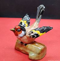 Front angled view of the goldfinch ceramic bird figurine on a red background