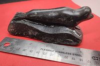 Side view of dark polished stone seal sculpture on textured base with measurement ruler showing approximately 5 inches.