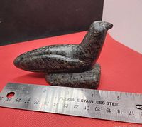 Side profile view of the dark stone bird carving with a stainless steel ruler showing length about 4.5 inches.