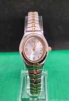 Front angle view of ladies quartz dress watch with two-tone metal expandable bracelet, white dial, and gold-tone hour markers and hands.