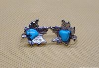 Pair of vintage silver-toned maple leaf earrings with central blue stones shown on textured background.