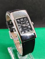 Front angled view of ladies rectangular quartz watch showing black dial with white Roman numerals, silver-tone case, and black leather strap